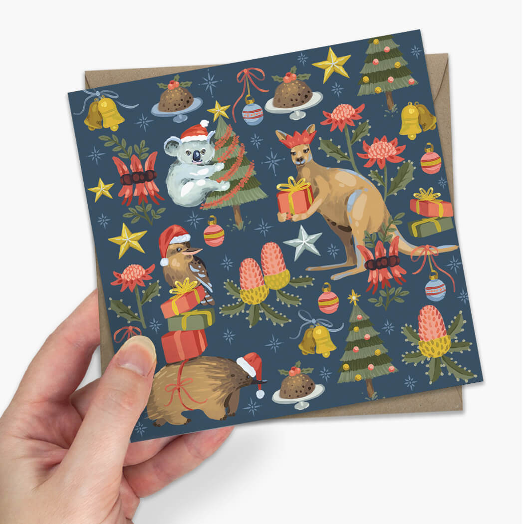  Christmas greeting card featuring festive Australian animals like a koala, kangaroo, emu, and echidna with Christmas decorations, alongside a brown envelope on a light gray background.