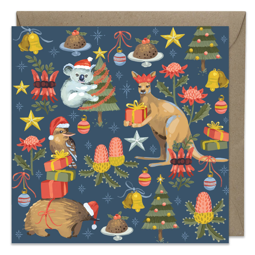 A square Christmas greeting card featuring a navy blue background with a festive illustrated pattern of kangaroos, a koala, a bird, Christmas trees, ornaments, stars, and desserts, shown with a brown kraft envelope behind it.