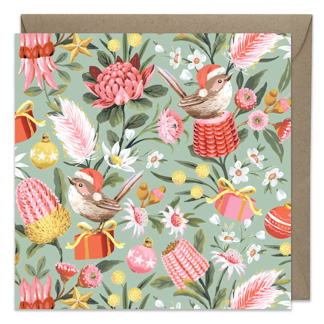 A square greeting card with a festive illustrated pattern of wrens, flowers, gifts, and ornaments on a pale green background, shown with a brown kraft envelope behind it.