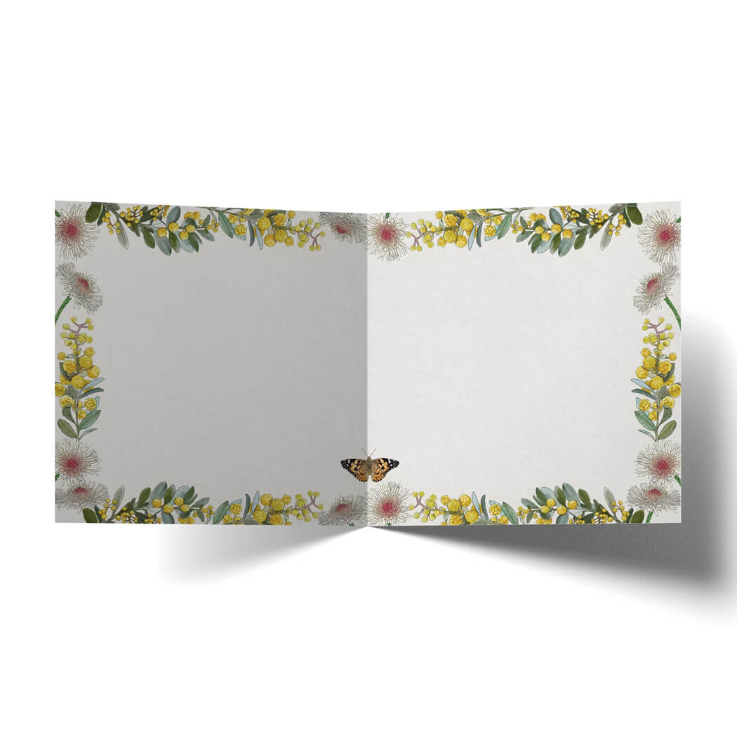 An open greeting card decorated with a border of yellow wattle green leaves, and small pink blossoms, plus a small butterfly near the bottom center